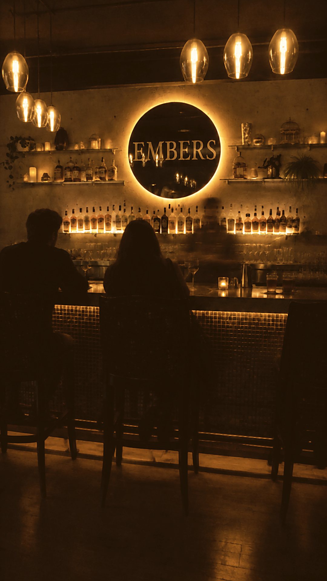 Le bar de l’Embers le soir, le miroir rond EMBERS illuminé au-dessus des bouteilles