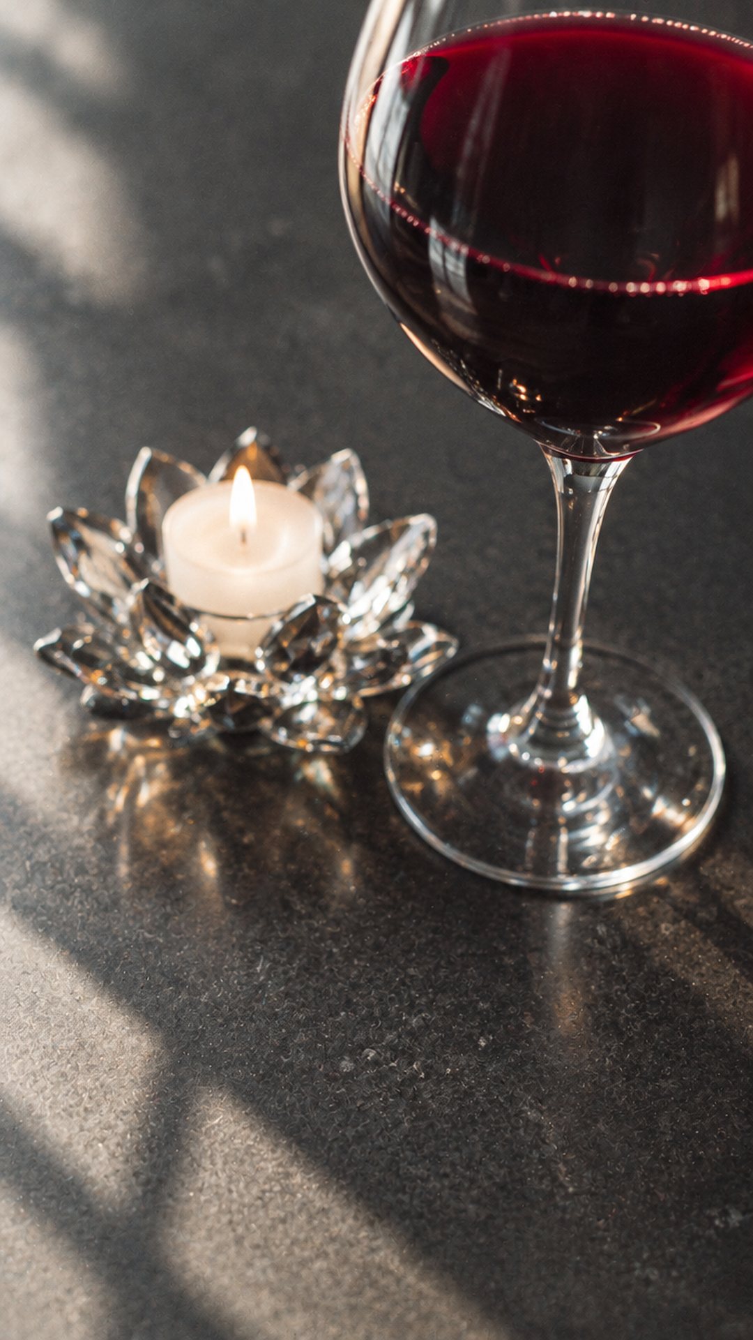 Un verre de vin rouge à côté de la bougie lotus en cristal du restaurant, sur une pierre sombre